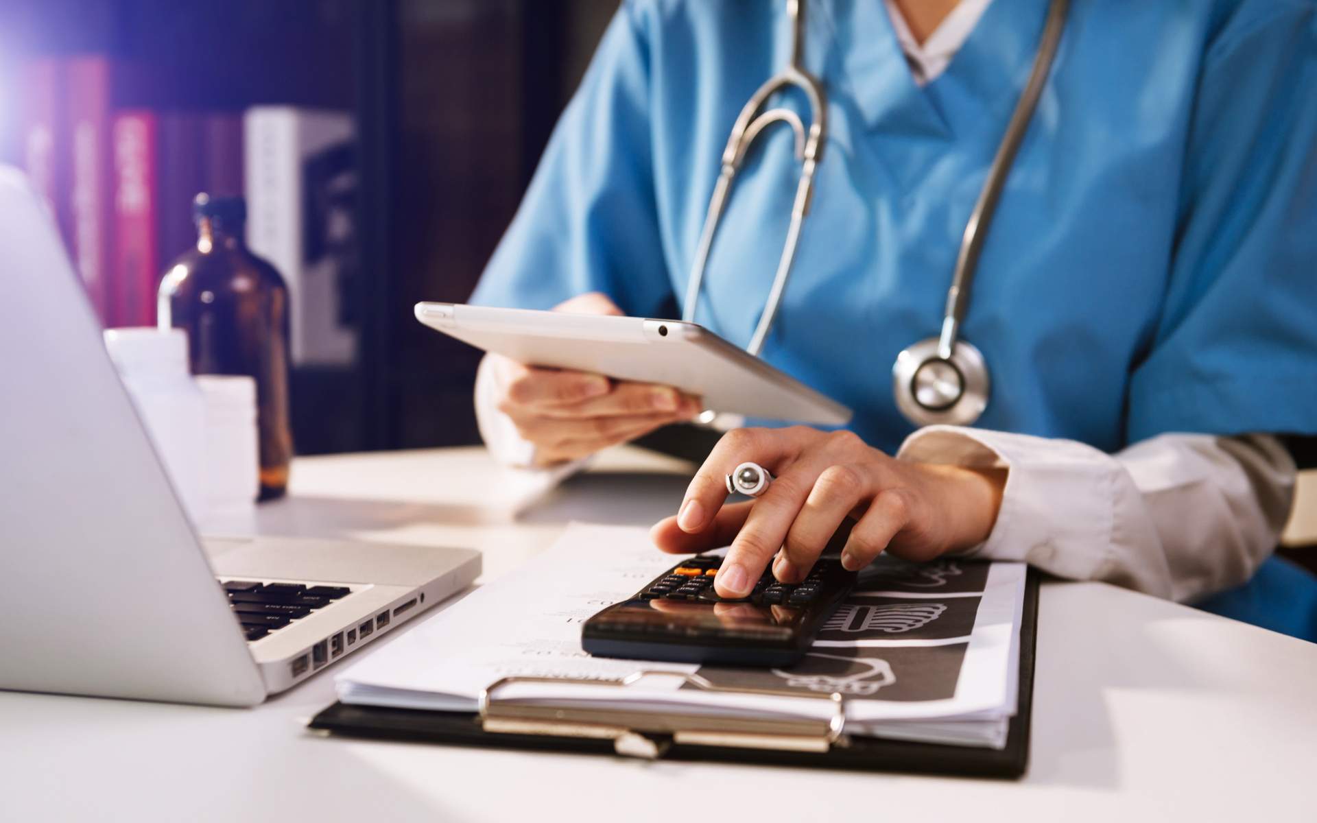 Image for Affordable Care Act Changes for 2023 and What to Expect in the 2023 Open Enrollment Period. An image of a doctor sitting at a desk with a laptop, tablet, and a calculator.