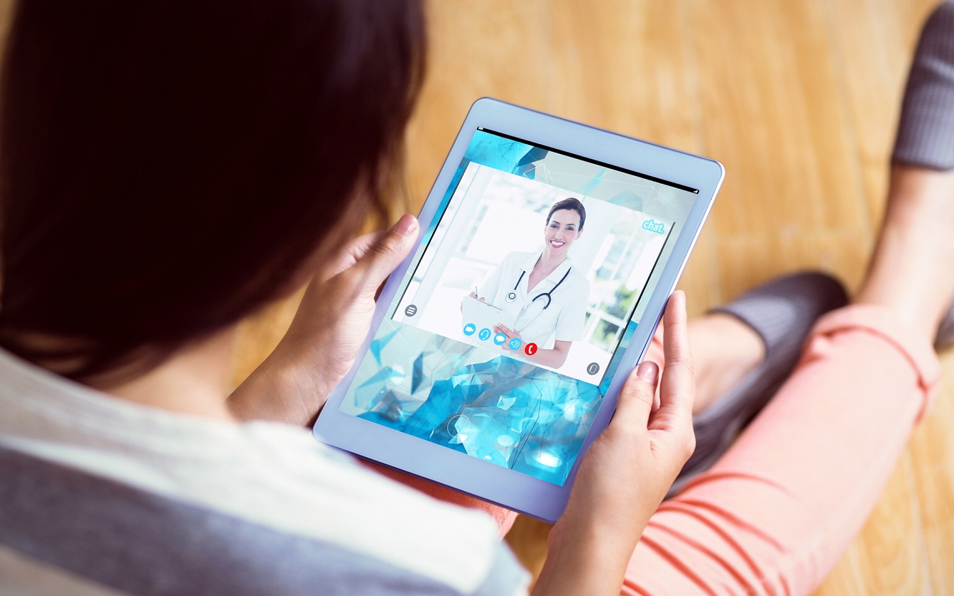 Image for How Tech Will Impact Healthcare in 2023. a person sits on the floor with a tablet having a telemedicine appointment.